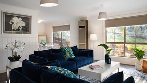 A modern living room with a dark blue sofa set, a white coffee table, and a large window with a view of greenery.