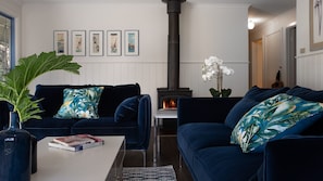A living room with two dark blue sofas, a white coffee table, a large green plant, and a fireplace.