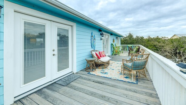 Een overdekt terras met rieten meubels en een blauwe balustrade.