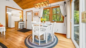 A dining area with a round table, white chairs, a wooden ceiling, and large windows with curtains. - A Relaxation Station (Morgantown)