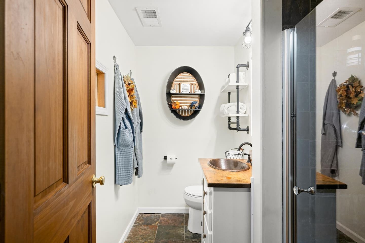 A bathroom with a wooden door, a toilet, a sink with a wooden countertop, a towel rack, and a shower area.