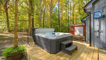 A hot tub on a wooden deck with a forest backdrop, a shed, and a safety sign.