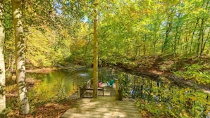 A wooden dock leading to a small bridge over a calm river, surrounded by dense trees and greenery. - A Relaxation Station (Morgantown)