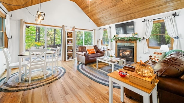 A cozy living room with a fireplace, wooden ceiling, and large windows offering a view of the outdoors. - A Relaxation Station (Morgantown)