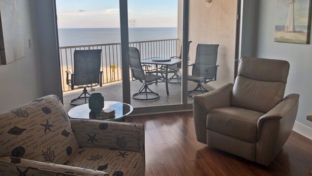 A room with a view of the sea, a balcony with outdoor furniture, and a painting on the wall.