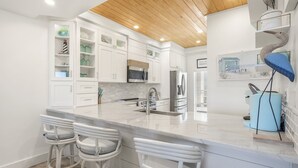 A modern kitchen with white cabinetry, a large island with bar stools, stainless steel appliances, and a wooden ceiling. - High Pointe Overlooking Lagoon Pool, Gulf Views! (Rosemary Beach)