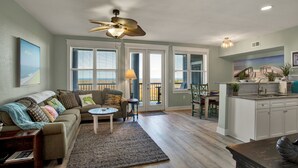 Un salon comprenant un canapé, une table basse et un ventilateur de plafond. Il y a également un coin cuisine avec un évier et des placards.