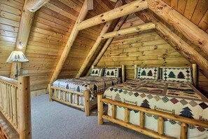 Ein gemütliches Schlafzimmer im Dachgeschoss mit Holzbalken, zwei Betten mit gemusterten Betttextilien und einer kleinen Lampe.