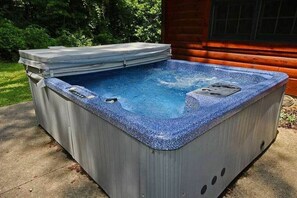 Ein Whirlpool mit Abdeckung vor einer Holzhütte.
