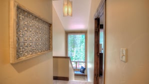 A hallway with a decorative wall panel, a staircase, a window with a view of trees, and a light fixture. - The Breckenridge Bicycle House - One Mile to Main St and the gondola (Breckenridge)