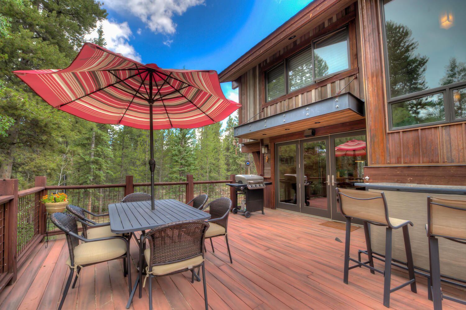 A wooden deck with a table and chairs, a grill, and a large umbrella.