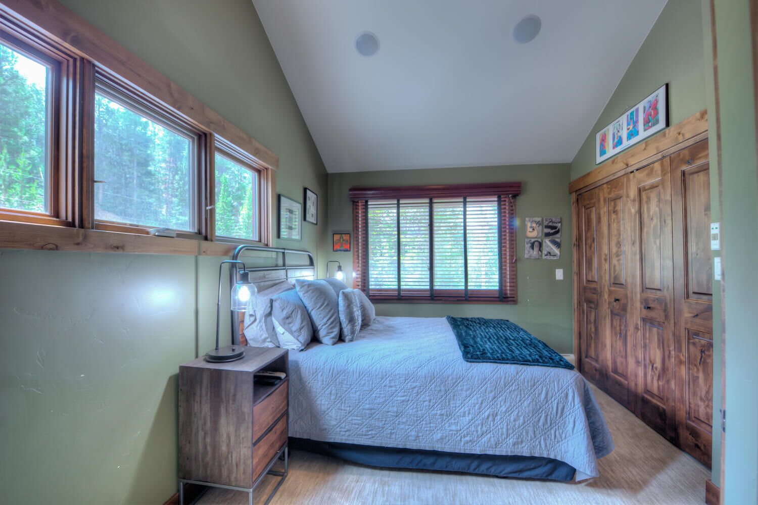 A bedroom with a bed, bedside table, lamp, and a window with blinds.