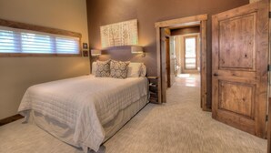 A bedroom with a large bed, a nightstand, a wall-mounted lamp, and a wooden door. - The Breckenridge Bicycle House - One Mile to Main St and the gondola (Breckenridge)