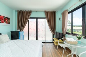 A hotel room with a bed, a desk, a chair, a TV, a small table with a basket, and a window with curtains.