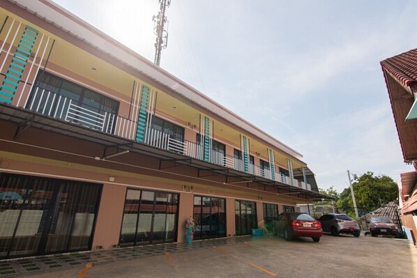 A multi-story building with balconies, a parking area, and a clear sky.