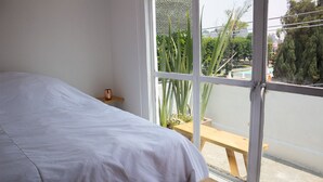 A bedroom with a bed, a wooden bench, and a window with a view of greenery and a pool. - 2 Bed in the heart of Cholula with views to the Pyramid and the (San Andrés Cholula)