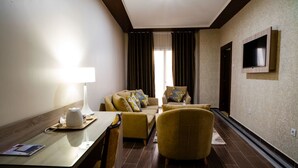 A hotel room with a sofa set, a dining table with a lamp, a TV mounted on the wall, and a patterned carpet. - Hôtel Tapis Rouge (Mila)