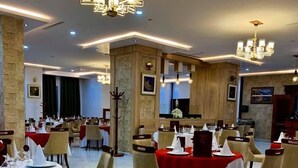 A spacious dining area with multiple tables set for service, featuring a modern chandelier and a stone accent wall. - Hôtel Tapis Rouge (Mila)