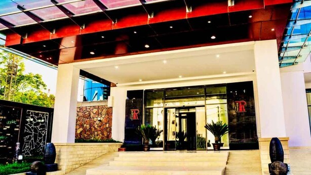 A hotel entrance with a modern design, featuring a glass facade, a stone wall, and a prominent 'R' logo. - Hôtel Tapis Rouge (Mila)