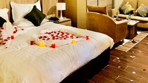 A hotel room with a large bed, a sofa, a nightstand with a lamp, and a small table with a bottle. - Hôtel Tapis Rouge (Mila)