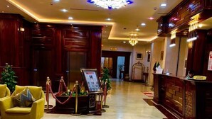 A hotel lobby with a reception desk, a yellow armchair, a red carpet, and a chandelier. - Hôtel Tapis Rouge (Mila)