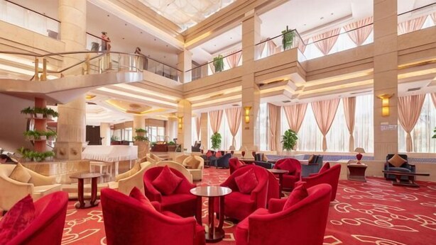 Un vestíbulo de hotel con asientos rojos, una mesa de centro y una escalera que conecta los pisos.