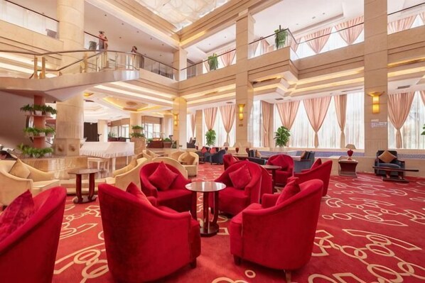 Un vestíbulo de hotel con asientos rojos, una mesa de centro y una escalera que conecta los pisos.