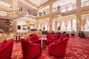 Um saguão de hotel com uma escadaria imponente, várias áreas de estar e teto alto.