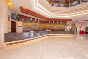 Un hall de hotel con un mostrador de recepción curvo, un cuadro grande en la pared y un diseño de techo moderno.