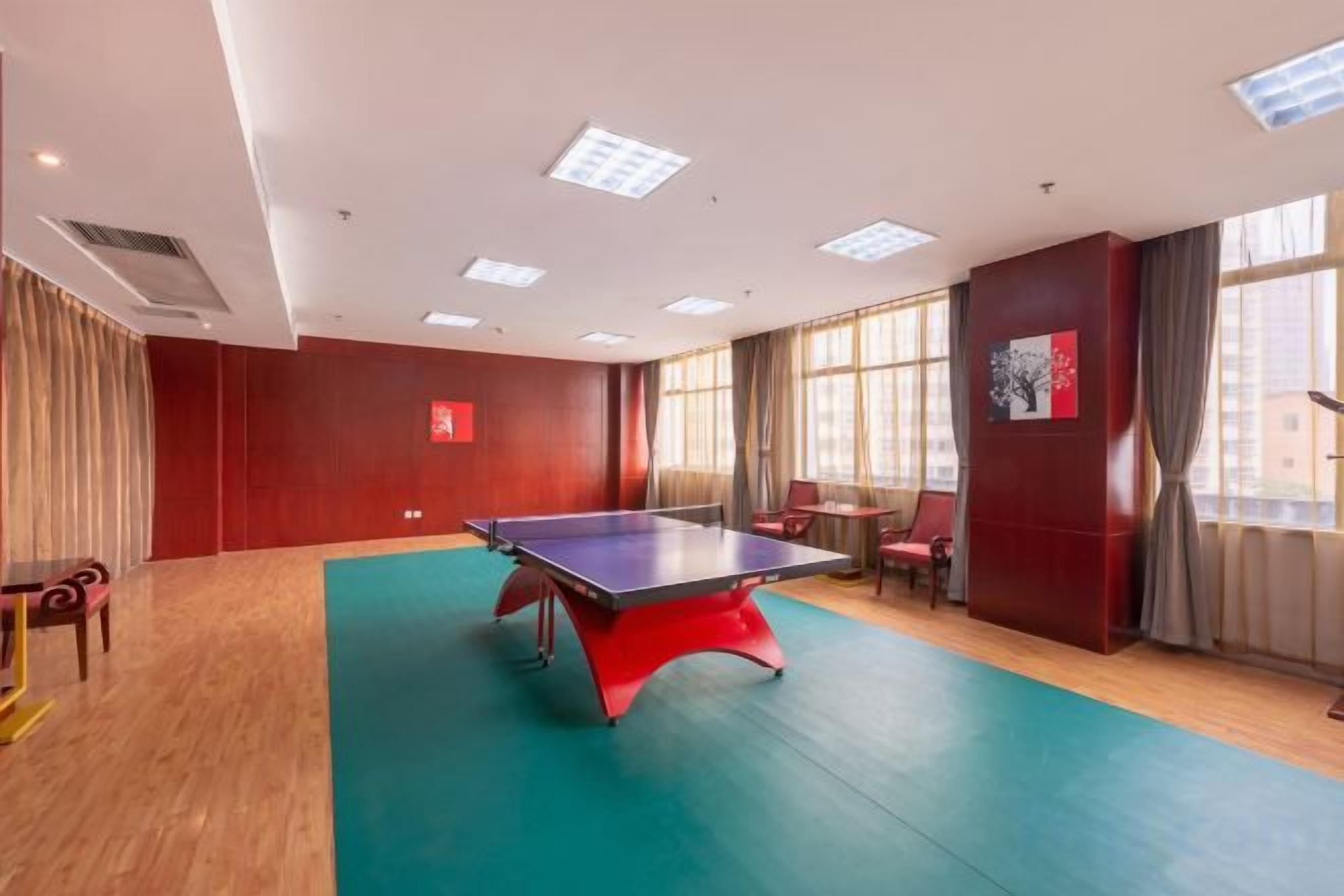 A room with a ping pong table, a red wall, and a window with curtains.