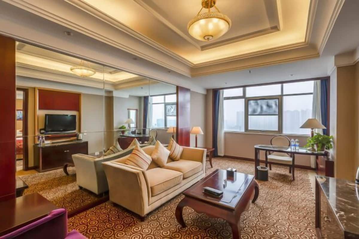 Habitación de hotel con sofá, mesa de centro, televisor y escritorio con lámpara.