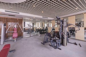 Un gimnasio con varios equipos de ejercicio, incluyendo cintas de correr y máquinas de pesas, y un espejo grande en la pared.