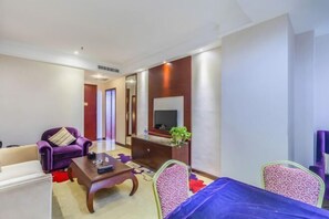 Una sala moderna con un sofá, un sillón y una mesita de centro. Hay un televisor montado en la pared y una planta pequeña en un estante.
