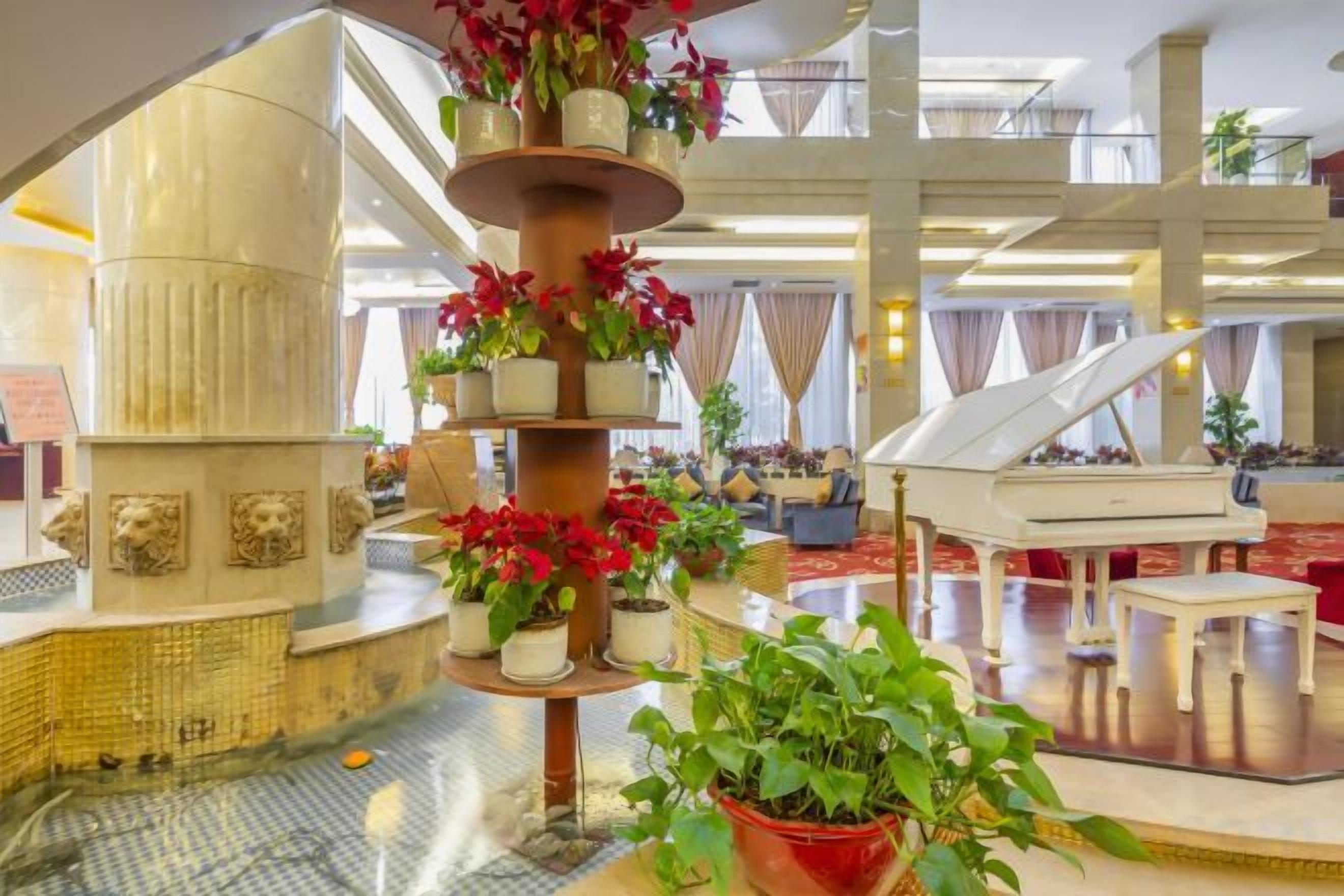A grand lobby with a central fountain, a grand piano, and potted plants.