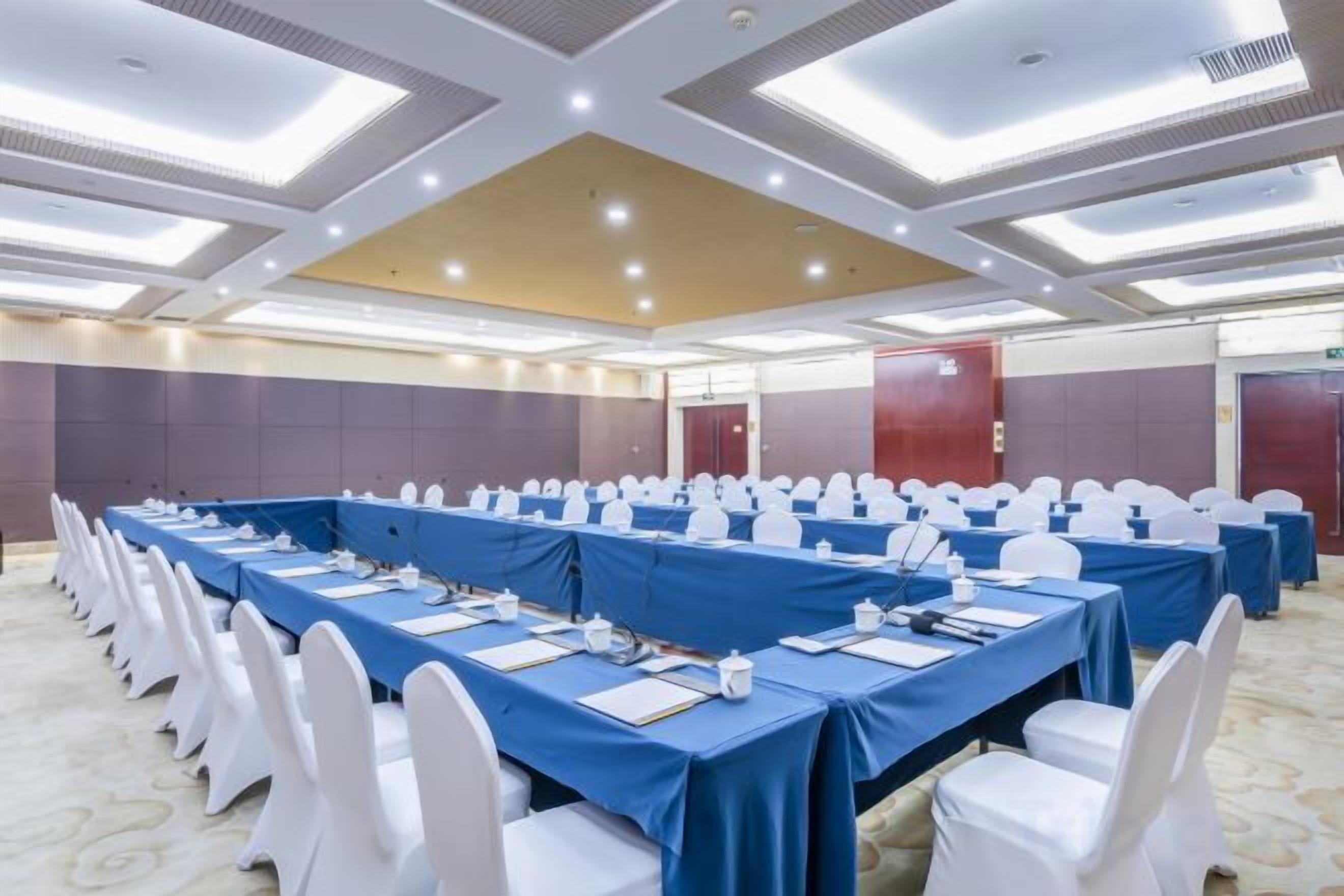 Un salón de conferencias con largas mesas, sillas blancas y piso alfombrado.