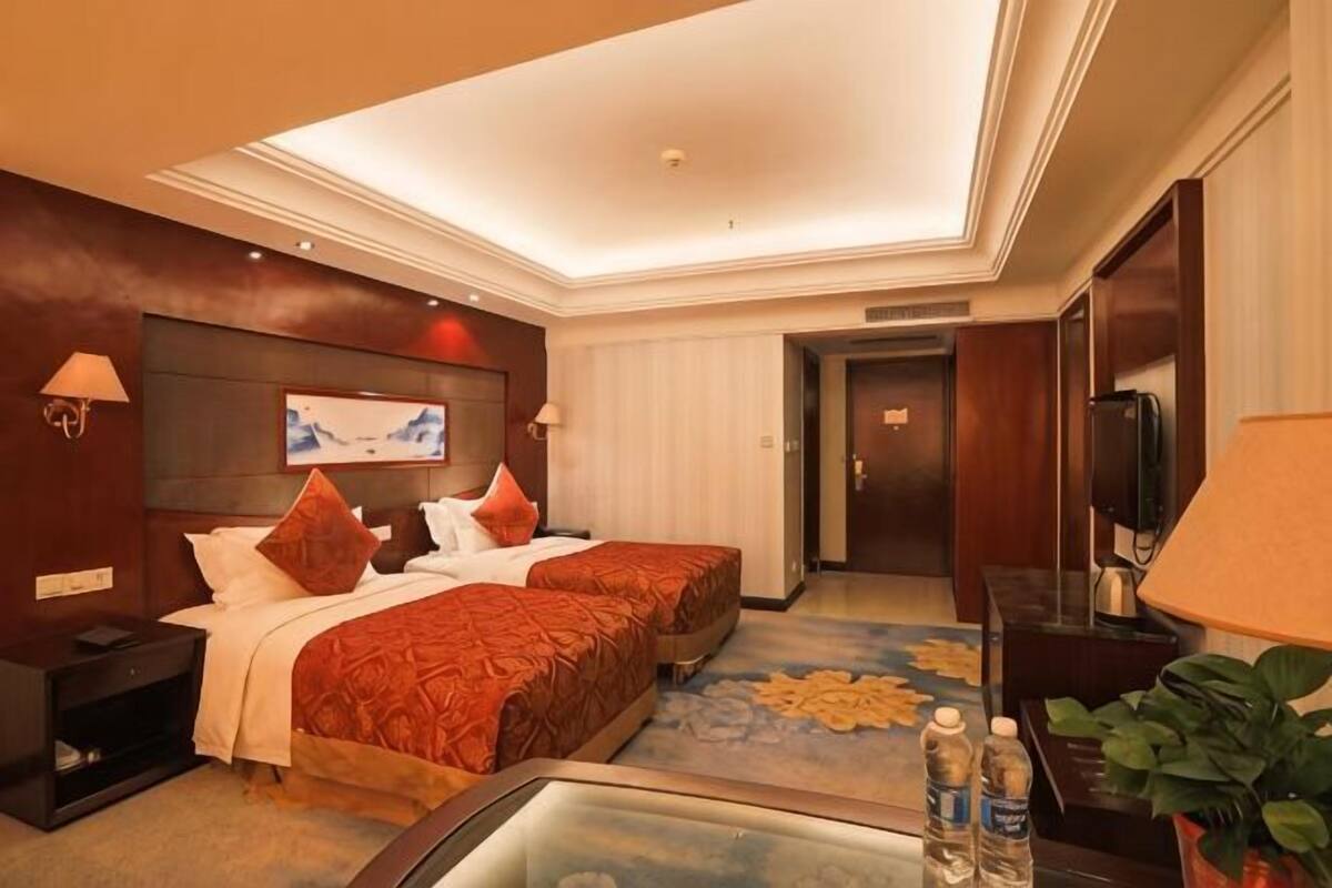 Habitación de hotel con dos camas, un televisor de pantalla plana, un escritorio con lámpara e iluminación en el techo.