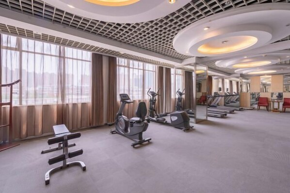 Un gimnasio amplio con máquinas de cardio, una banca y un muro de espejos.