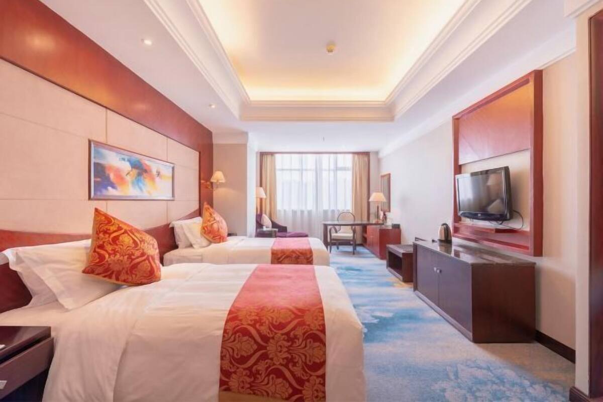 Una habitación de hotel con dos camas, televisión, escritorio y ventana.