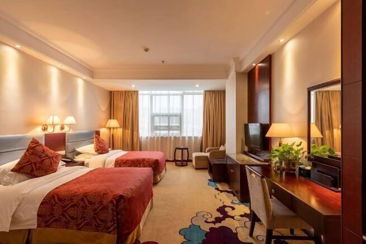 Una habitación de hotel con dos camas, un escritorio, un televisor y un ventanal grande.