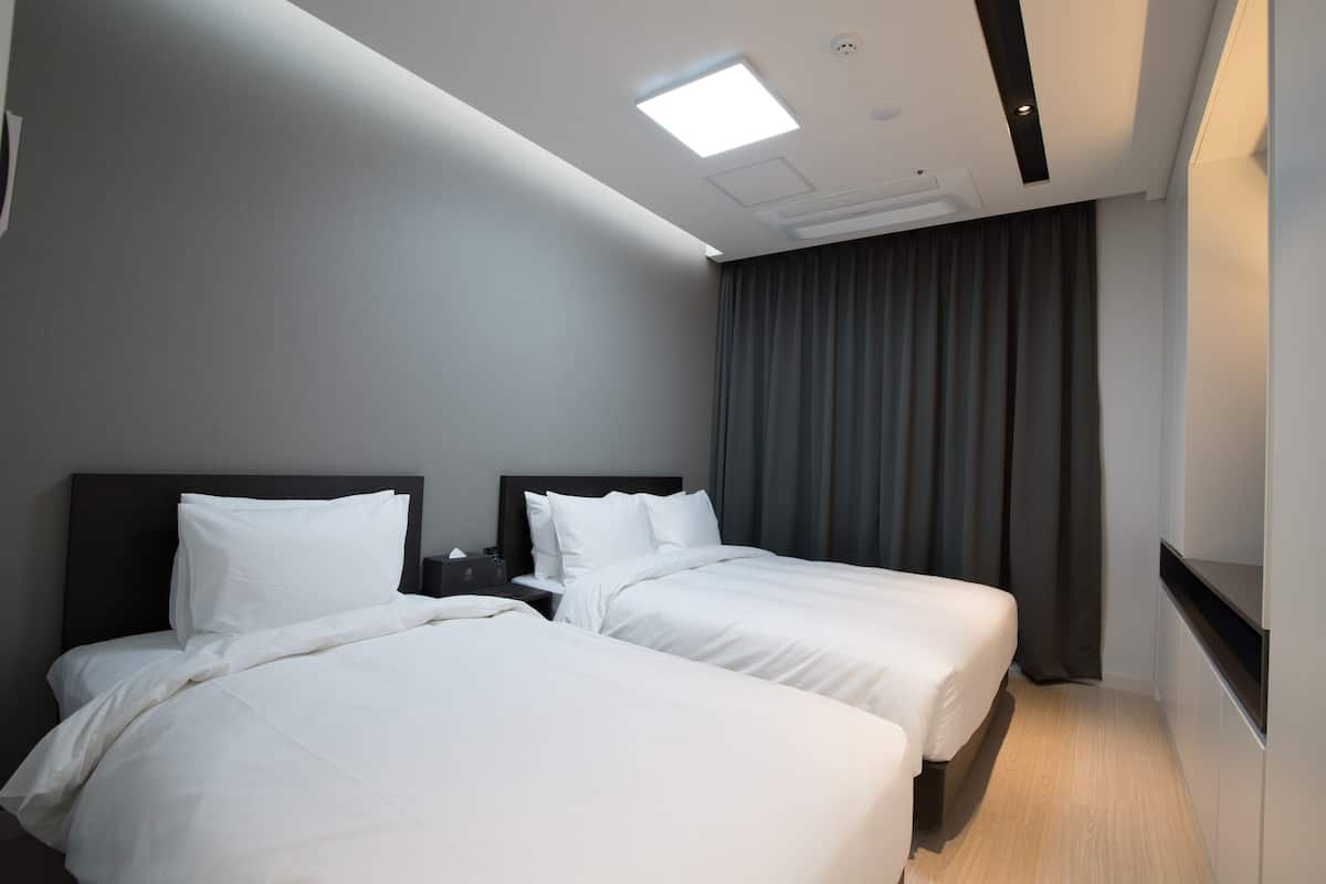 A hotel room with two beds, a flat-screen TV, a desk, and a ceiling light.
