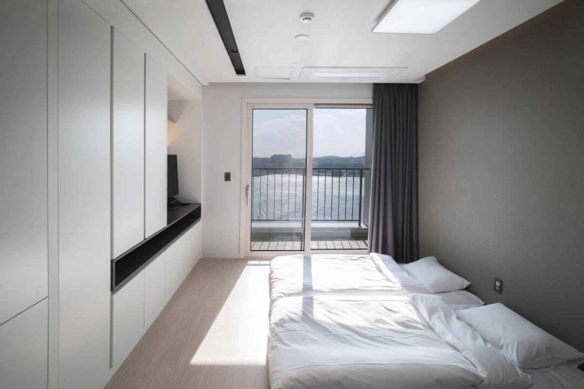 A modern hotel room with a large bed, a TV, and a balcony with a view of the water.