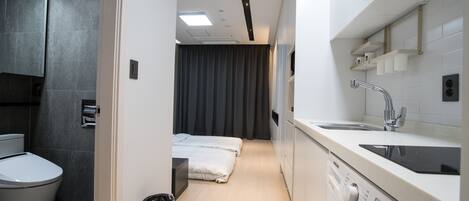 A compact hotel room with a shower, toilet, bed, and a washing machine.