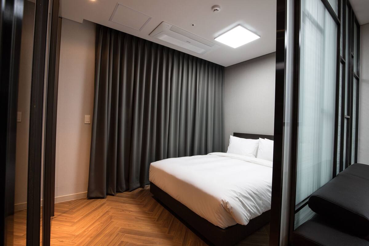 A modern hotel room with a large bed, dark curtains, and a wooden floor.