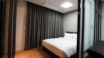 Quarto de hotel moderno com uma cama grande, cortinas escuras e piso de madeira.