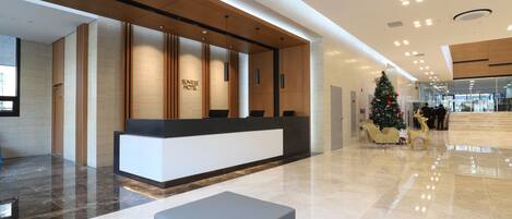 A modern hotel reception area with a reception desk, a Christmas tree, and a seating area.