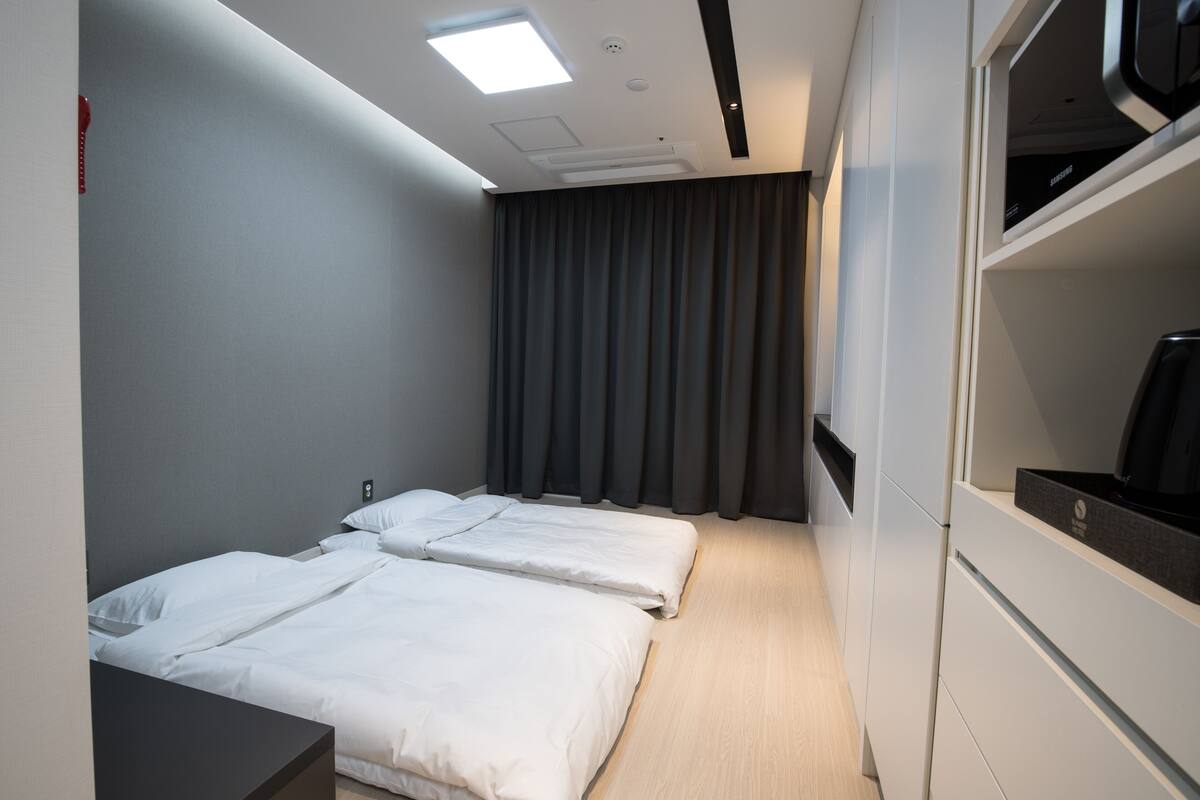 A hotel room with two single beds, a desk, a wardrobe, and a large window with curtains.