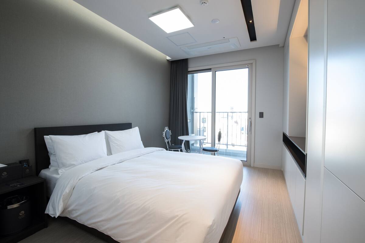 A modern hotel room with a large bed, a small table, and a balcony with a view.