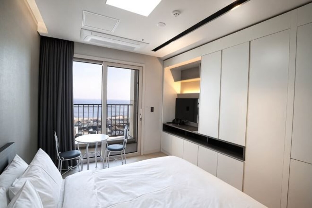 A hotel room with a bed, a small table with chairs, a TV, and a balcony with a view.