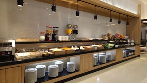 En buffet med forskellige retter, en kaffemaskine og stablede tallerkener.