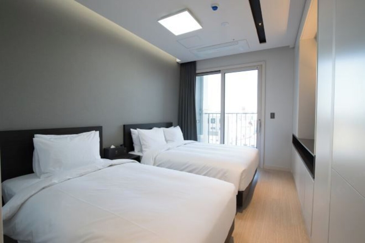 A hotel room with two beds, a large window, and a modern ceiling design.